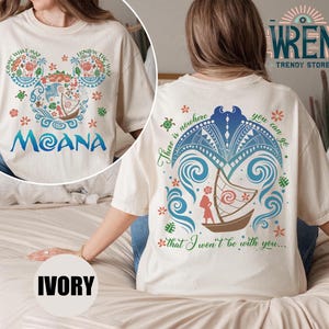 May include: A white t-shirt with a colorful design of a boat and waves on the back. The front of the shirt has a Mickey Mouse head design with the words "Come What May" and "Know The Way" on the ears. The word "Moana" is printed below the Mickey Mouse head. The shirt is available in ivory.