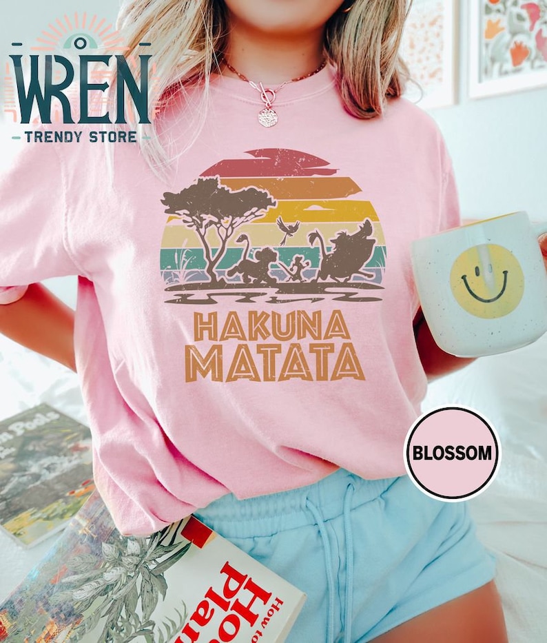 May include: A pink t-shirt with a vintage sunset graphic featuring the Lion King characters Simba, Timon, and Pumbaa. The text "Hakuna Matata" is printed below the graphic.