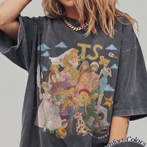 May include: A charcoal gray oversized t-shirt featuring a graphic print of various animated characters dressed in diverse outfits, including a space suit, cowboy gear, and gowns. The text TS appears at the top, and the bottom right reads Comfort Colors Pepper.