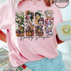 May include: Pink t-shirt with a Halloween-themed graphic featuring cartoon characters in costumes, pumpkins, and the text "Spooky Season." The shirt is from Wren Trendy Store.