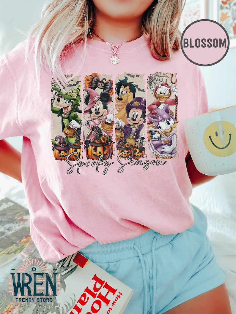 May include: Pink t-shirt with a Halloween-themed graphic featuring cartoon characters in costumes, pumpkins, and the text "Spooky Season." The shirt is from Wren Trendy Store.
