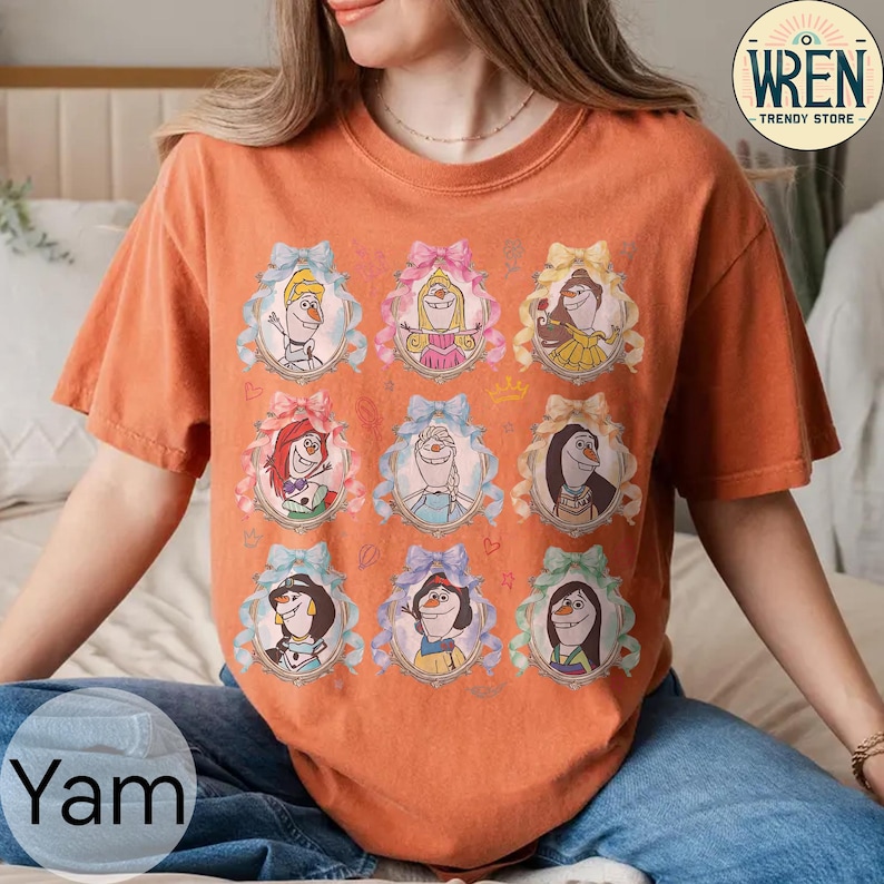 Puede incluir: Camiseta naranja de manga corta con nueve retratos enmarcados de personajes de dibujos animados. Cada retrato est&aacute; en un marco ovalado con un lazo. Los lazos son azules, rosas y amarillos. La camiseta tiene el texto "Yam" en la parte inferior izquierda.