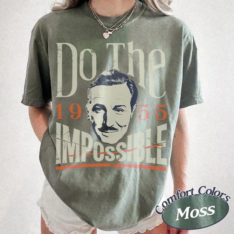 May include: Olive green t-shirt with the text "Do The Impossible" and a portrait of a man. The number "1955" is above the portrait, and the word "Impossible" is below, with a line through it. The shirt has a "Comfort Colors Moss" label.