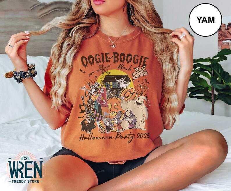 Puede incluir: Camiseta naranja con un dise&ntilde;o tem&aacute;tico de Halloween. El dise&ntilde;o presenta personajes, una casa embrujada, calabazas y el texto "Oogie Boogie Bash Halloween Party 2025". La camiseta tiene un corte holgado.