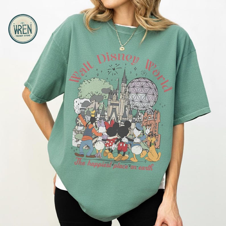 以下が含まれることがあります： ディズニーワールドのグラフィックが特徴の緑色のTシャツ。デザインには、ミッキーマウス、ミニーマウス、ドナルドダック、グーフィー、象徴的なランドマークが含まれています。「ウォルト・ディズニー・ワールド」と「世界で一番幸せな場所」というテキストがあります。