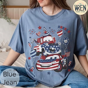 Puede incluir: Camiseta azul vaquero con un dise&ntilde;o patri&oacute;tico con coches de dibujos animados, estrellas y fuegos artificiales. El dise&ntilde;o incorpora los colores rojo, blanco y azul, con el n&uacute;mero "95" en un globo y un coche. La camiseta tiene un corte holgado.