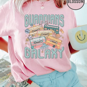 K&ouml;nnte beinhalten: Rosa T-Shirt mit einem Aufdruck von Kassetten und dem Text "Guardians of the Galaxy".