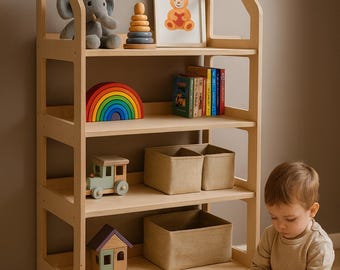 May include: A light wood children's bookshelf filled with toys, including a stuffed elephant, a wooden rainbow, and a framed bear picture. A child is playing with wooden blocks on the floor. The bookshelf has four shelves and two side panels.
