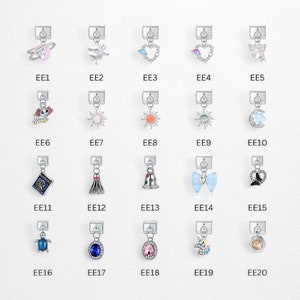 May include: A collection of silver-toned charms with various designs, including a planet, a bird, a heart, a butterfly, a dog, a sun, a moon, a book, a dress, a bell, a bow, a turtle, and gemstones. Each charm is labeled with an "EE" followed by a number.
