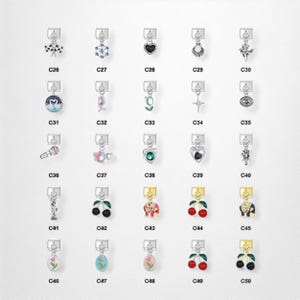 May include: A collection of silver-toned charms with various designs, including a heart, a cherry, a microphone, and an elephant. Each charm has a small loop at the top for attachment. The charms are labeled with the letters "C" and numbers.