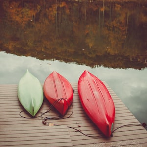 two red and green canoes sitting on a dock next to a lake