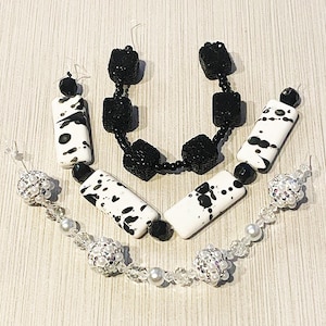 May include: A collection of handmade jewelry pieces, including earrings, a necklace, and a bracelet. The earrings and necklace feature black and white rectangular beads with a spotted pattern. The bracelet has clear beads and pearl accents.