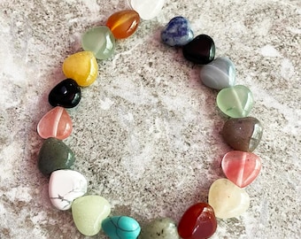 May include: A strand of heart-shaped gemstones in various colors, including white, orange, green, yellow, black, pink, gray, turquoise, and red. The gemstones are strung together on a clear string, creating a unique and colorful accessory.