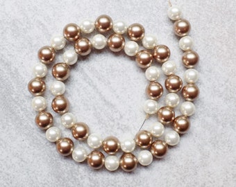 May include: A strand of white and gold pearl beads. The beads are strung on a thin wire and are arranged in a circular pattern.