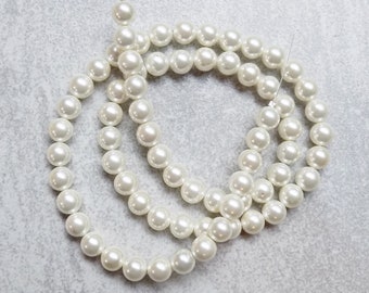 May include: A strand of white faux pearl beads. The beads are round and smooth, and they are strung on a thin wire. The beads are arranged in a loose, flowing pattern.