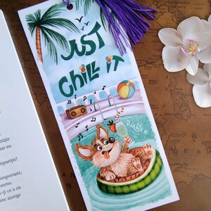 May include: A whimsical bookmark featuring a cartoon corgi dog relaxing in a watermelon float in a pool. The bookmark has the text "Just Chill It" and a purple tassel. A beach ball and palm trees are also depicted.
