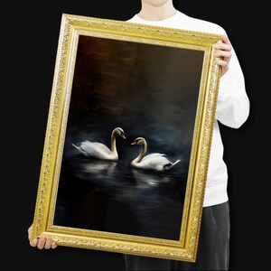 May include: A framed painting featuring two white swans on a dark, reflective body of water. The swans face each other, their necks curved. The ornate gold frame adds a classic touch to the artwork.