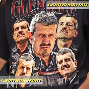 May include: Black t-shirt featuring multiple images of a man with short gray hair and a goatee. The word "GUENTHER" is printed in red and white above the man's name, "Steiner", in white script.