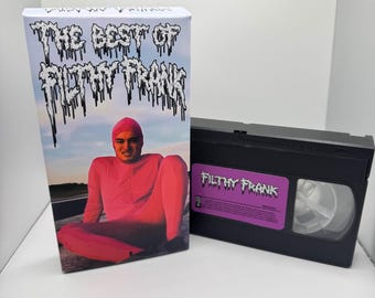 May include: A VHS tape and box set featuring the text "THE BEST OF FILTHY FRANK." The box art shows a person in a pink bodysuit and beanie. The VHS tape has a purple label with the text "FILTHY FRANK."