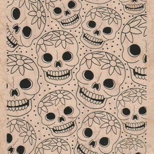 May include: A woodblock stamp with a repeating pattern of black and white sugar skulls with floral designs. The skulls have large eyes and a toothy grin.