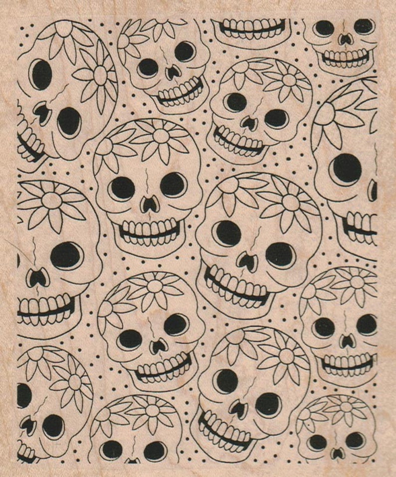 May include: A woodblock stamp with a repeating pattern of black and white sugar skulls with floral designs. The skulls have large eyes and a toothy grin.