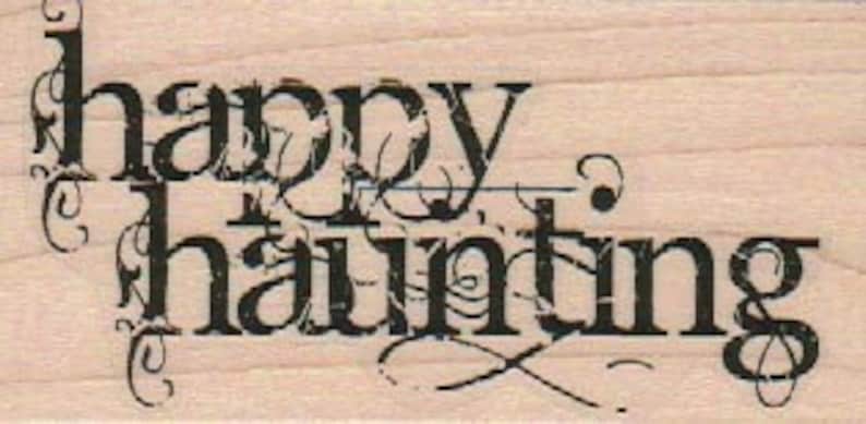 Puede incluir: Un sello de goma de estilo vintage con el texto "happy haunting" en una fuente negra con adornos decorativos.
