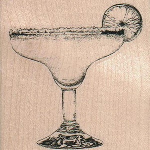 Könnte beinhalten: Ein Glas Margarita-Glas mit einem gesalzenen Rand und einem Limettenkeil am Rand. Das Glas ist mit einer hellgelben Flüssigkeit gefüllt.