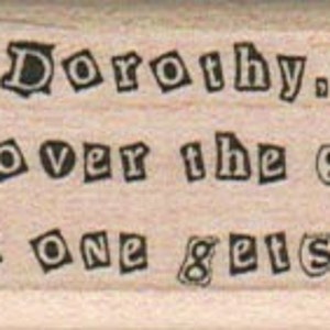 Może przedstawiać: Drewniana pieczątka z napisem "Dorothy. Hand over the shoes and no one gets hurt!" w czarnym kolorze. Tekst jest napisany zabawną czcionką na jasnobrązowym tle drewna.