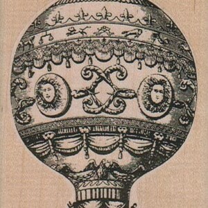 May include: A detailed black and white illustration of a hot air balloon. The balloon features ornate designs, including sun-like faces, decorative swags, and animal figures. The balloon's shape is rounded at the top and tapers towards the base.