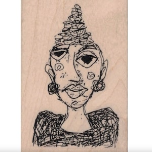 Puede incluir: Un dibujo lineal en blanco y negro de una cara con un estilo único. La cara tiene ojos grandes, una nariz pequeña y una boca detallada. La figura lleva pendientes y un tocado. El dibujo está sobre un bloque de madera de color claro.