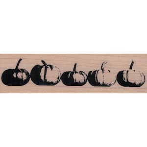 May include: A wooden stamp featuring five stylized black pumpkin illustrations. Each pumpkin has a stem and is arranged horizontally. The pumpkins vary slightly in their shading and detail, creating a rustic, seasonal design.