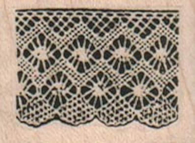 Op de afbeelding: Een close-up van een vintage kantversiering met een herhalend patroon van kleine cirkels en ruiten. De kant is wit en heeft een delicaat, ingewikkeld ontwerp.