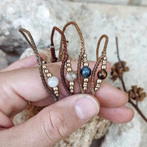 Peut inclure: Cinq bracelets en cordon marron et perles dorées, chacun avec une perle de pierre précieuse de couleur différente. Les perles sont blanches, brunes, bleues et brunes.