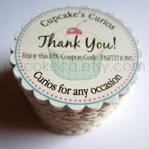 May include: A stack of cupcake-shaped tags with a scalloped edge. The tags feature a cupcake illustration and the words "Thank You!" in a script font. Text includes "Cupcake's Curios" and "Curios for any occasion."