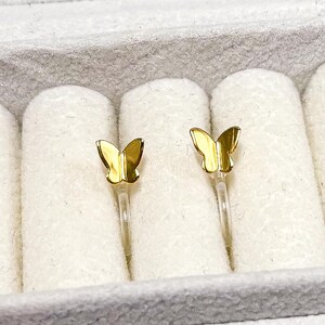 May include: A pair of gold butterfly earrings in a white jewelry box.