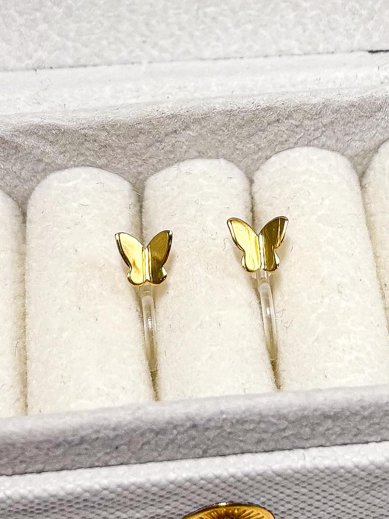 May include: A pair of gold butterfly earrings in a white jewelry box.