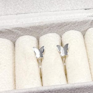 May include: A pair of silver butterfly earrings in a white velvet jewelry box.