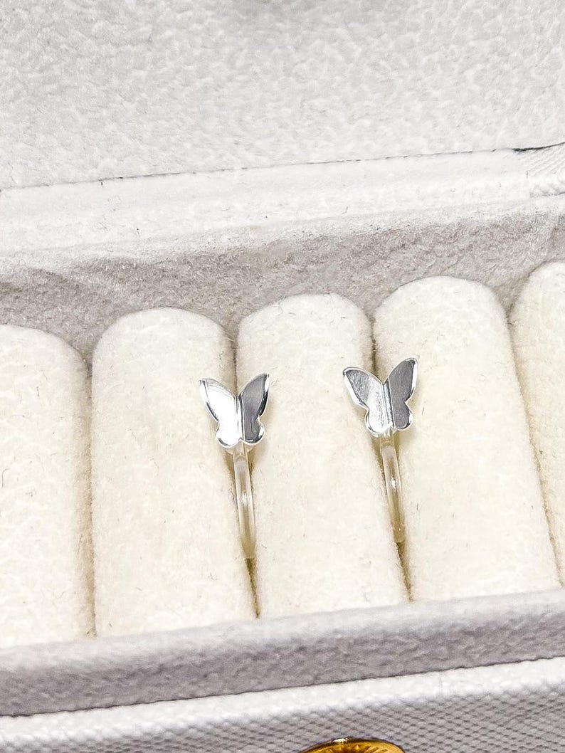May include: A pair of silver butterfly earrings in a white velvet jewelry box.