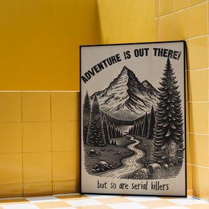 May include: Black framed art print with a mountain and forest landscape illustration. The text reads "ADVENTURE IS OUT THERE! but so are serial killers."