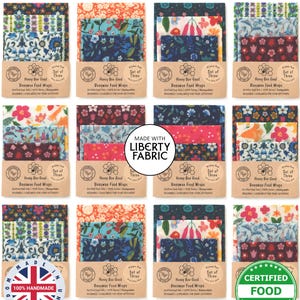 Puede incluir: Un conjunto de envoltorios de alimentos de cera de abeja con diseños florales. Cada juego de tres envoltorios se presenta en una funda de cartón. Los envoltorios están etiquetados como "Honey Bee Good" y "Certified Food Safe". La imagen también incluye el texto "Made with Liberty Fabric".