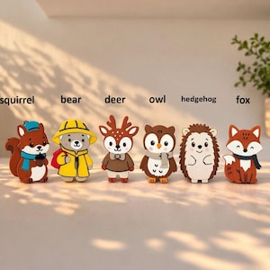 May include: Six cartoon animal figurines are displayed: a squirrel, bear, deer, owl, hedgehog, and fox. Each figure is brightly coloured and has a unique outfit or accessory. The figurines are arranged in a row on a white surface.