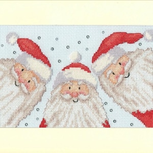 Könnte beinhalten: Kreuzstich-Stickerei mit drei lächelnden Weihnachtsmännern mit roten Mützen und weißen Bärten vor hellblauem Hintergrund mit weißen Punkten. Das Kunstwerk ist gerahmt.