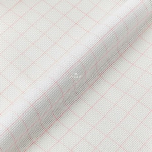 May include: White Aida cloth with a pink grid pattern. The cloth is folded and has a slight texture.