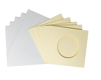 Op de afbeelding: Een pak van 10 witte enveloppen van karton met een rond uitsparing en een pak van 10 gele enveloppen van karton met een rond uitsparing.