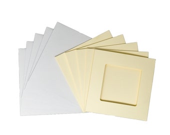 Op de afbeelding: Een verzameling witte en crèmekleurige passe-partouts en achterplaten. De passe-partouts hebben een vierkante opening in het midden. De items zijn in een waaier vorm gerangschikt, waarbij de passe-partouts en platen elkaar overlappen.