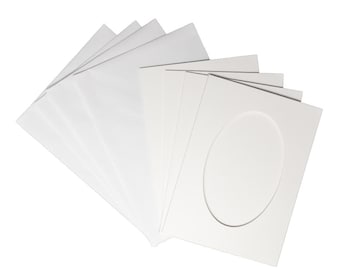 Op de afbeelding: Een stapel witte passe-partouts met ovale openingen. De passe-partouts zijn gemaakt van dik papier en zijn in een waaier gerangschikt. Ze zijn schoon en helder, met een glad oppervlak.