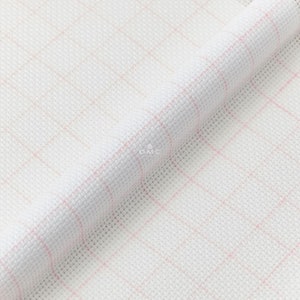May include: White Aida cloth with a pink grid pattern. The cloth is folded in half, showing the texture of the fabric.