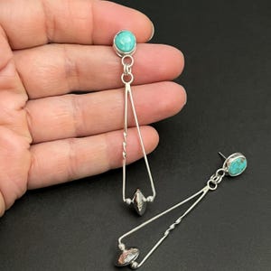 May include: A pair of silver dangle earrings with turquoise stones. The earrings feature a twisted wire design and a small silver bead at the bottom.