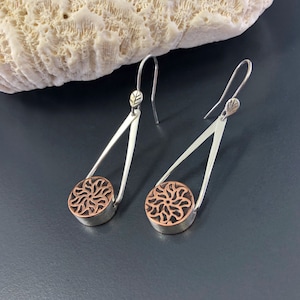Earrings featuring hand fabricated, mixed metal, copper, and sterling silver flower design beads dangling from sterling silver wire settings. Ear wires are sterling silver with hand-forged leaf detail.