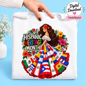 May include: A white sweatshirt featuring a graphic of a person with long brown hair wearing an off-the-shoulder top and a wide skirt composed of various national flags. The text reads Hispanic Heritage Month in colorful, bold lettering.